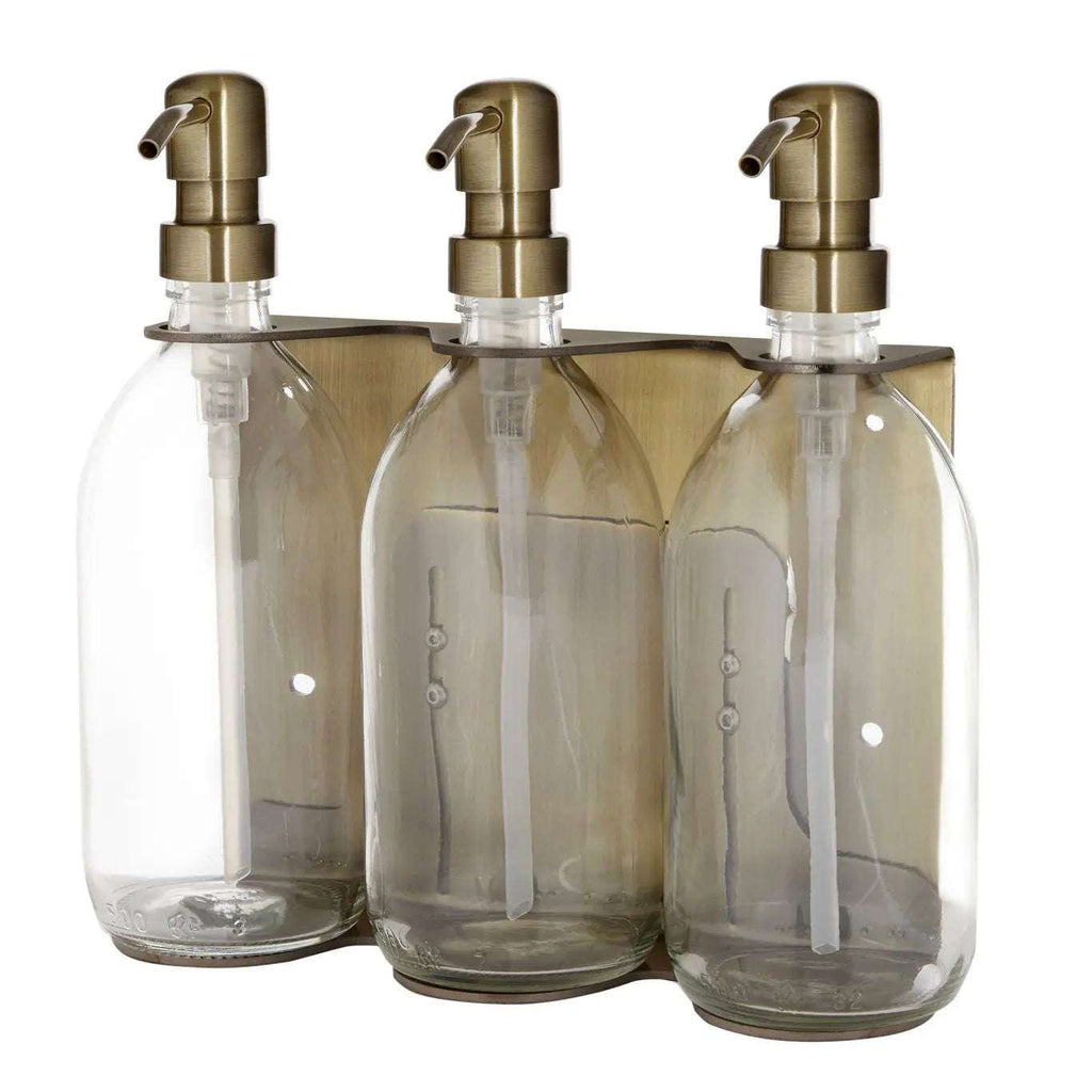 Triple distributeur de savon mural avec flacons verre transparent et pompe dorée.