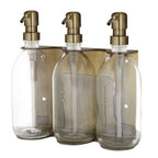 Triple distributeur de savon mural avec flacons verre transparent et pompe dorée.