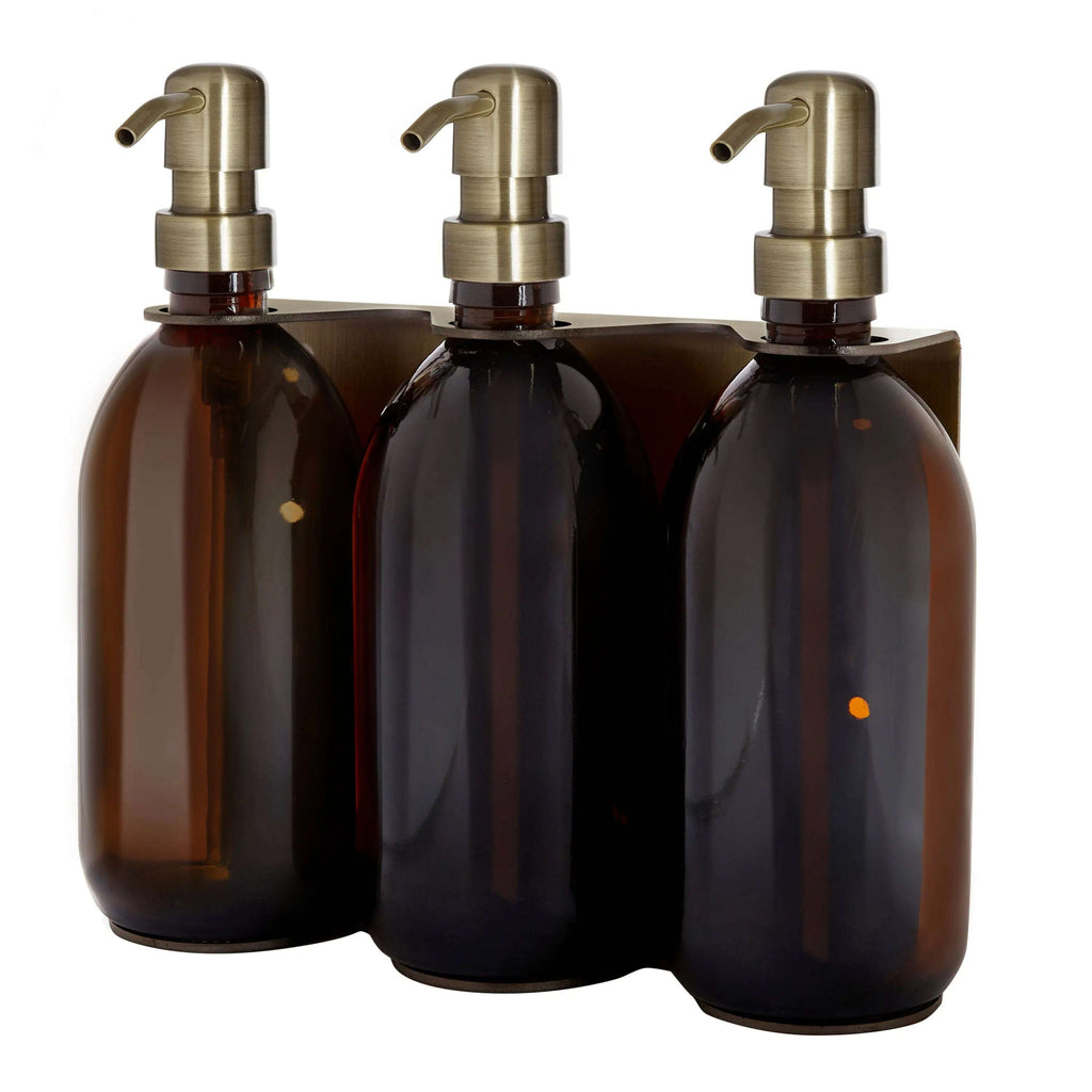 Triple distributeur de savon mural avec flacons verre ambré et pompe dorée.